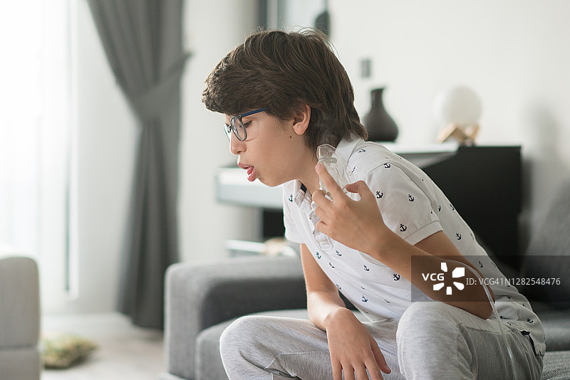 生病的男孩在家咳嗽并拿着面罩吸入器图片素材