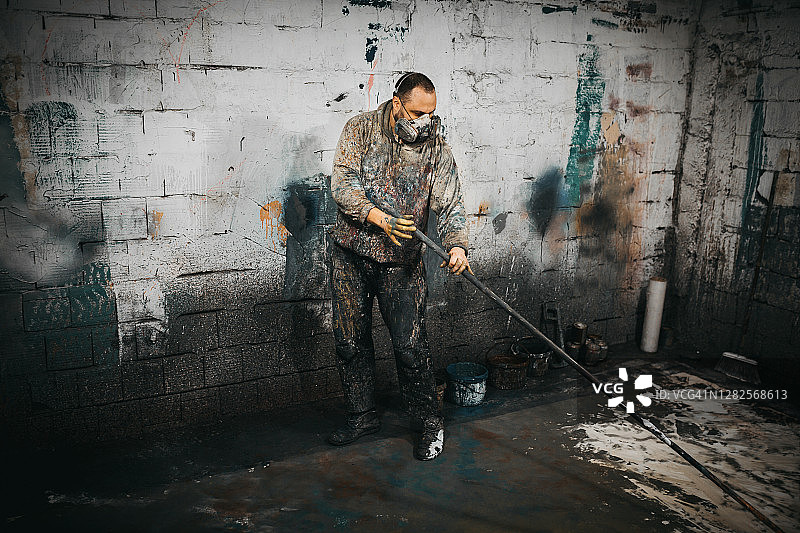 一名戴着防毒面具的男子在一个凌乱的房间里拿着一个长长的油漆滚筒图片素材