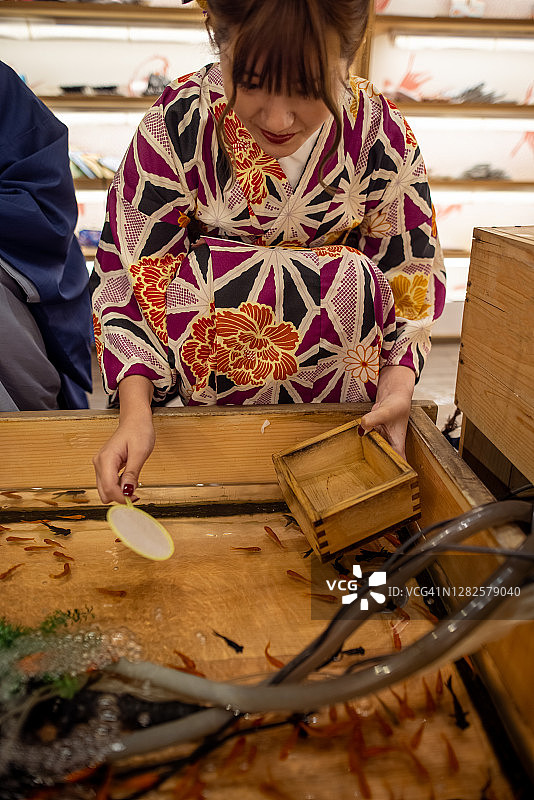 穿着和服的年轻女子在祭典上捞金鱼图片素材