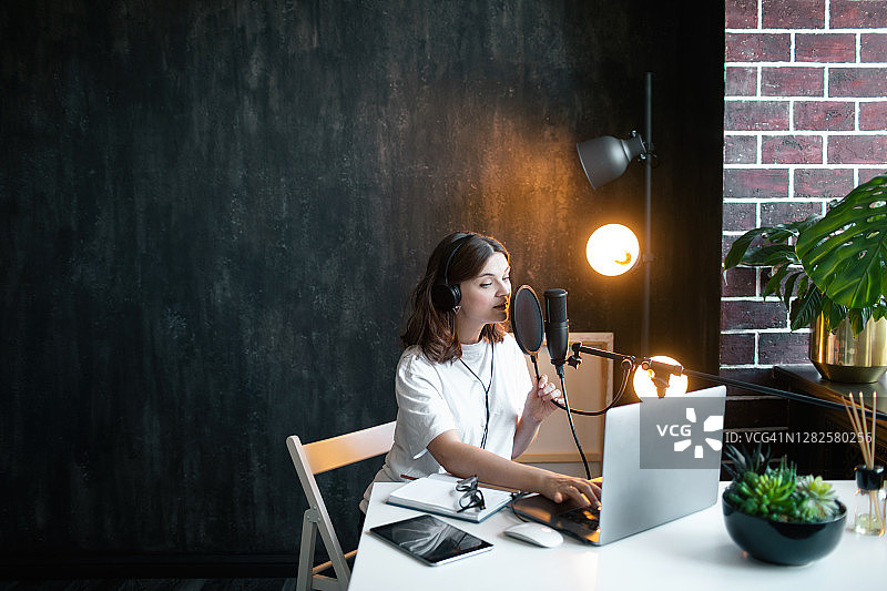 年轻女子戴着黑色耳机在家录制播客。图片素材