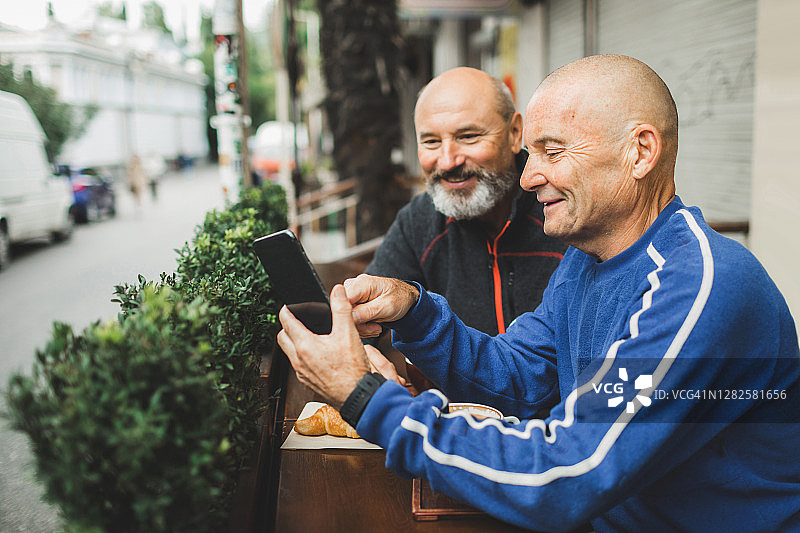 两位老年朋友在室外咖啡馆露台上喝咖啡并看智能手机图片素材