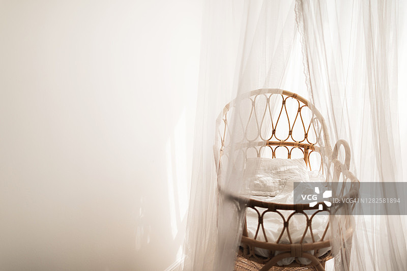 时尚的斯堪的纳维亚风格新生儿婴儿房，配有天然藤制摇篮和白色天篷图片素材