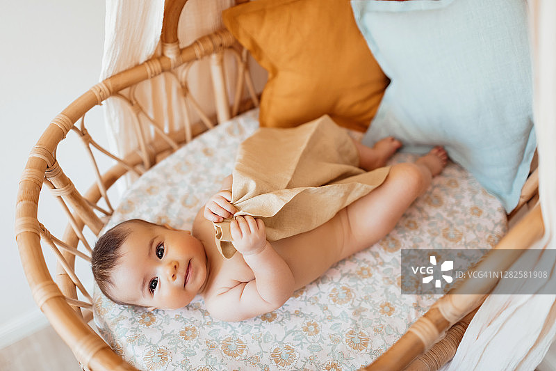 瞌睡的男孩在舒适的藤条婴儿床里打盹，家里有顶棚和枕头。高角度的婴儿女孩躺在星形垫子上天然亚麻床上。有机和天然纺织品的概念。图片素材
