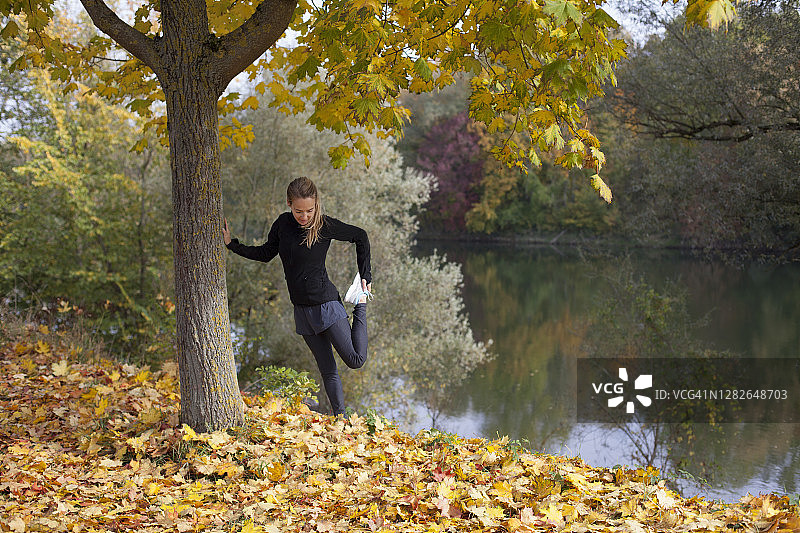 跑步后，女子倚靠在树上伸展腿部图片素材