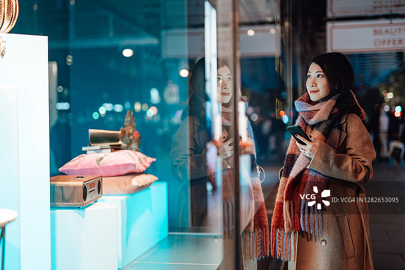 年轻女子在城市夜间橱窗购物图片素材
