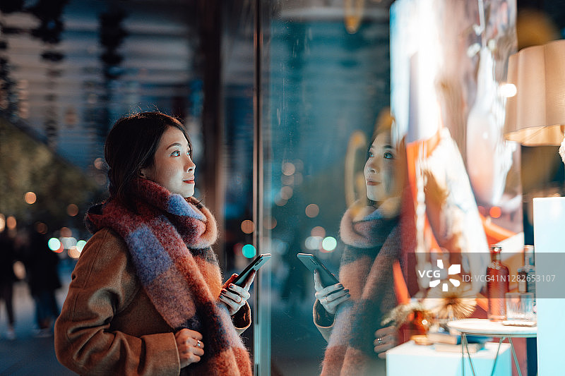 年轻女子在城市夜间橱窗购物图片素材