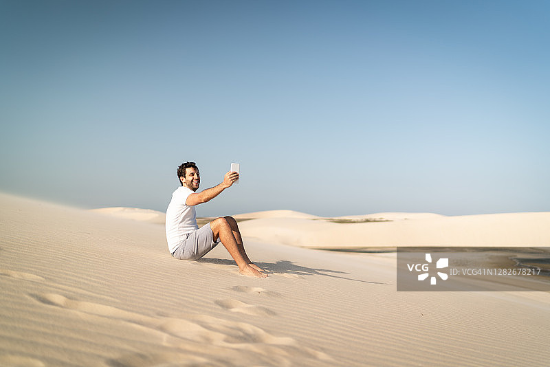 在杰里科科拉，沙丘上的男人用智能手机自拍/进行视频通话图片素材