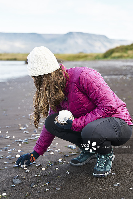 年轻女子在秋天的海滩上收集贝壳图片素材
