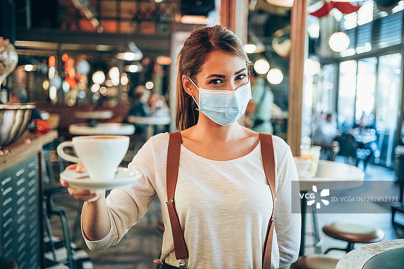 戴防护口罩在城市咖啡馆工作的漂亮女服务员图片素材