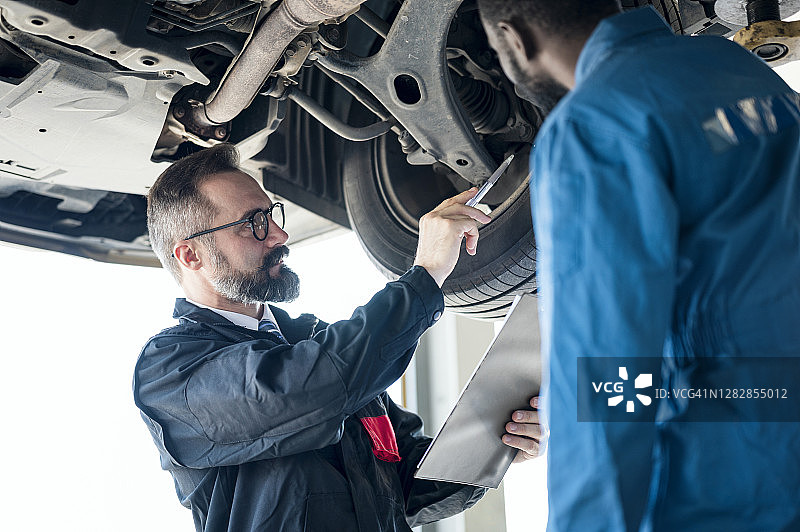 服务质量：汽车修理中心，汽车修理经理和机械师一起检查汽车底盘悬挂系统图片素材