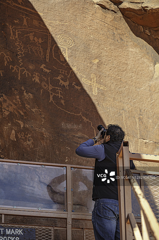 一名男子正在拍摄一块布满岩画的著名岩石图片素材