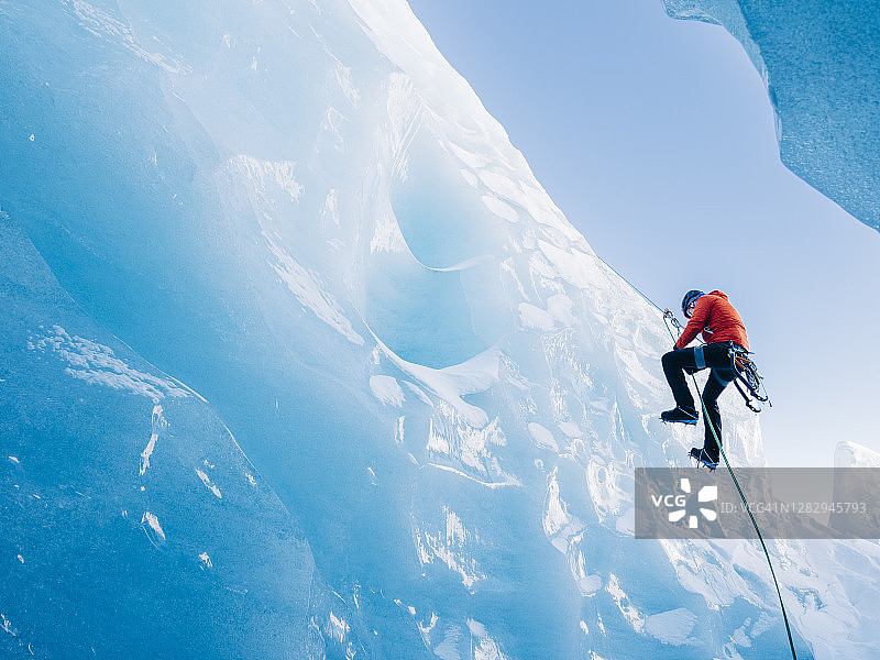 一名攀冰者顺着垂直的蓝色冰面下降到冰川的裂缝中图片素材