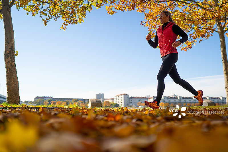 微笑的中年妇女在秋叶上慢跑图片素材