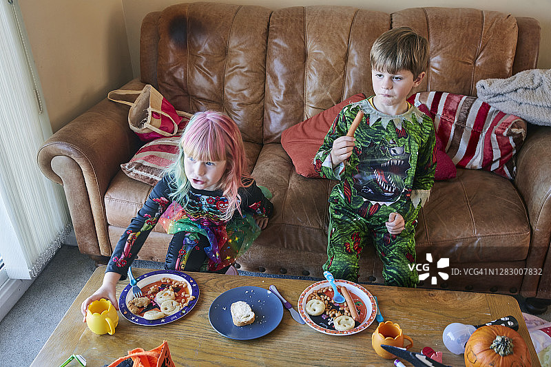 男孩和女孩穿着万圣节服装看电视吃东西图片素材