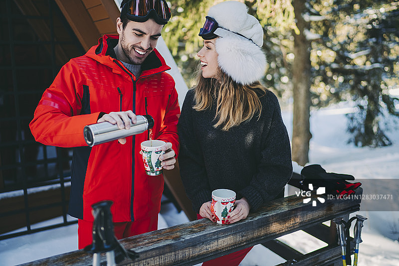 情侣在冬季假期于度假别墅的阳台上喝热茶图片素材