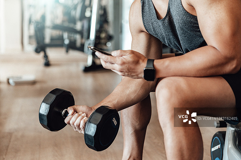 在健身房用智能手机训练的健壮青年图片素材
