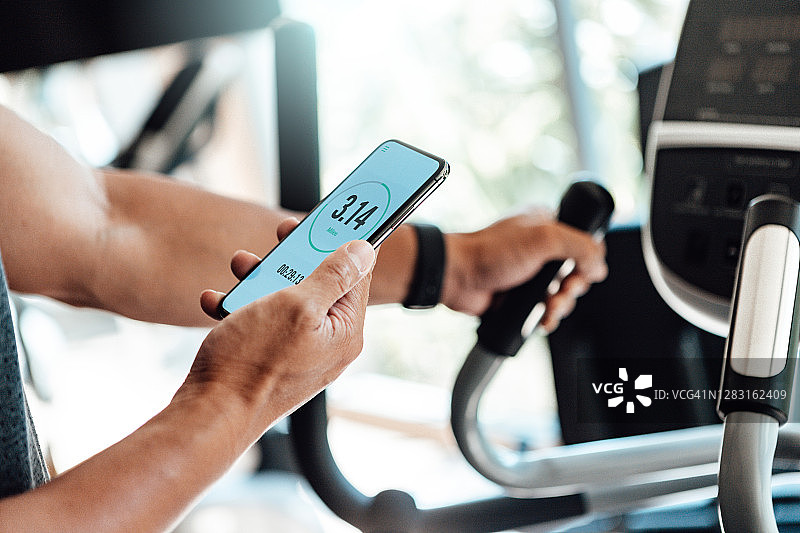 年轻男子在健身房使用椭圆机锻炼，同时使用智能手机图片素材