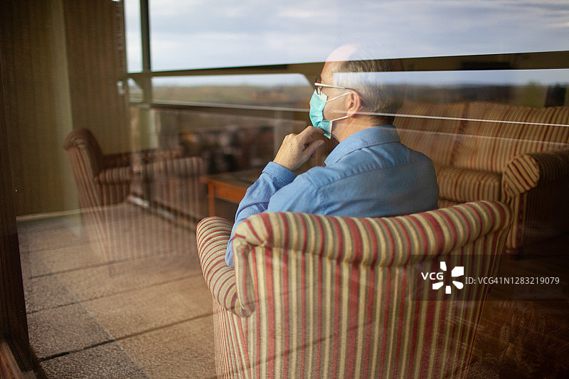 隔着窗户拍摄的，独自在家戴口罩的男子速写图片素材