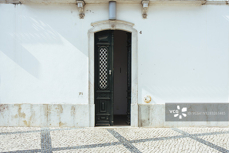 葡萄牙塔维拉，精美老式格栅门通向鹅卵石街。图片素材