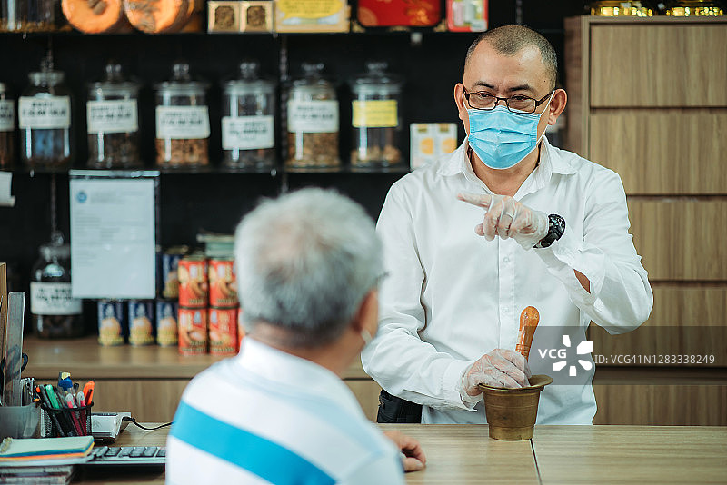 华人男药剂师在中药店柜台协助老年顾客图片素材
