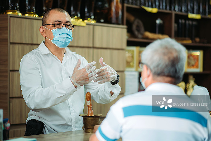 华人男药剂师在中药店柜台协助老年顾客图片素材