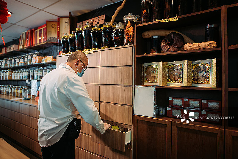 亚洲华人男药剂师在中药店挑选包装中草药图片素材