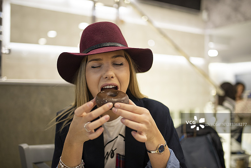 戴着时髦帽子的漂亮女人正在吃可可甜甜圈，因为她需要摄入巧克力图片素材