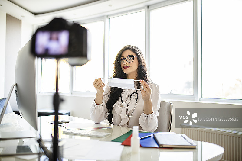 年轻女医生在她的博客上提供一些医疗建议，并展示如何在冠状病毒大流行期间使用防护口罩图片素材