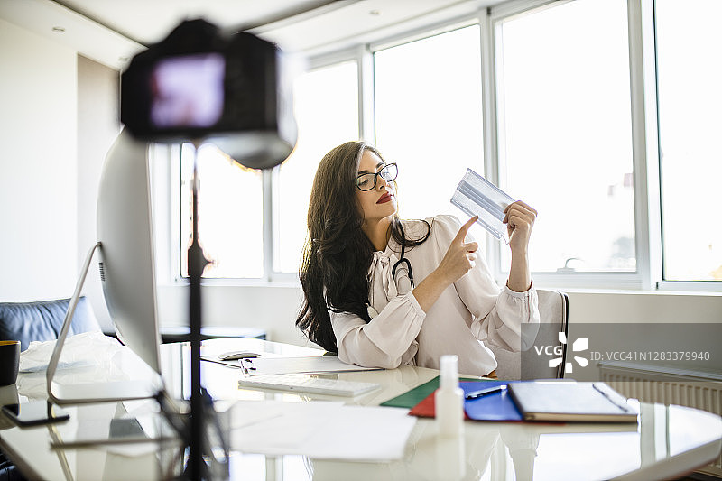 年轻女医生在她的博客上提供一些医疗建议，并展示如何在冠状病毒大流行期间使用防护口罩图片素材