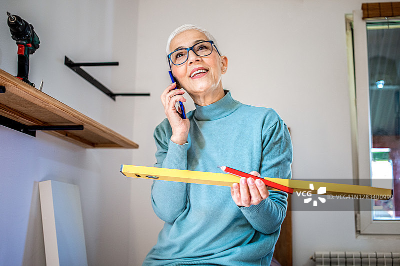 中年女人在公寓里挂架子并打电话图片素材