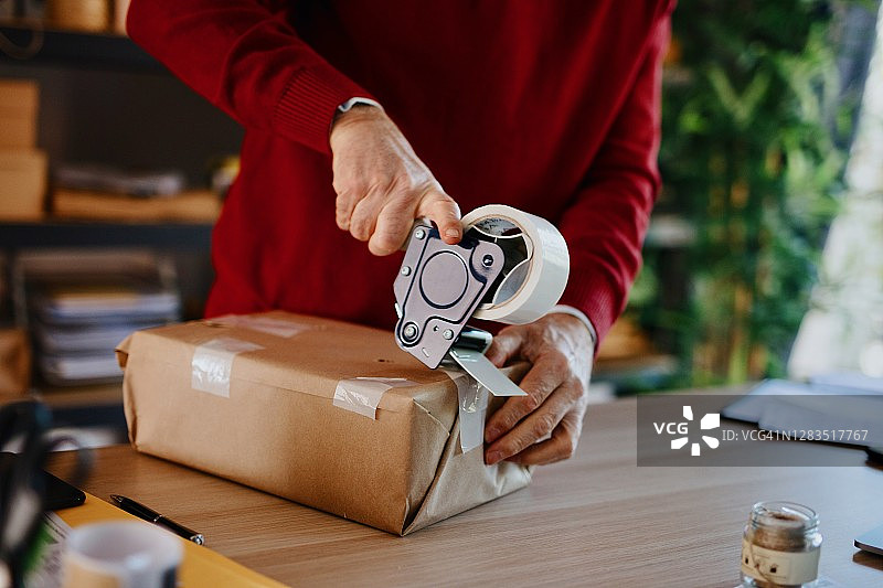 年长的男人拿着包装机，用胶带密封纸箱图片素材