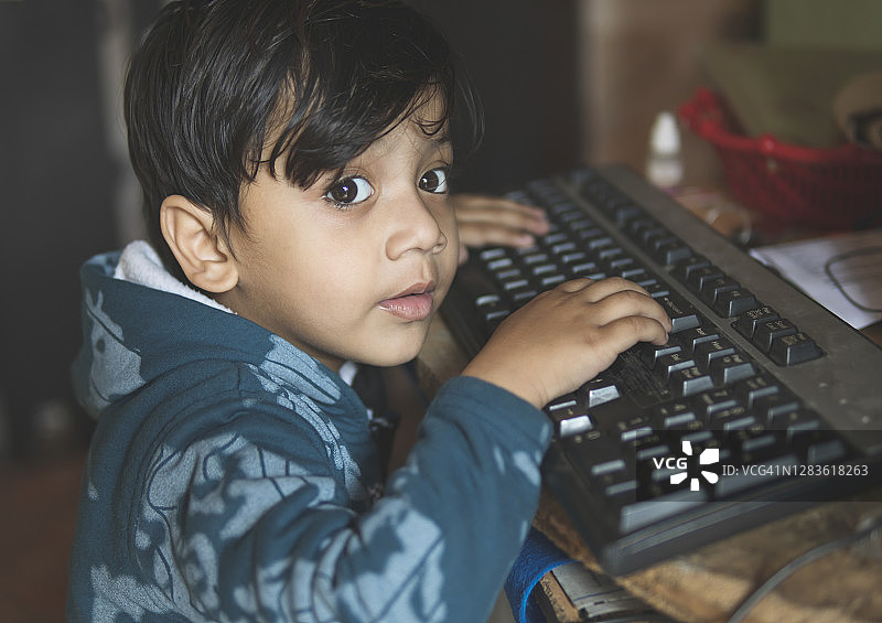 小男孩在电脑键盘上打字。图片素材