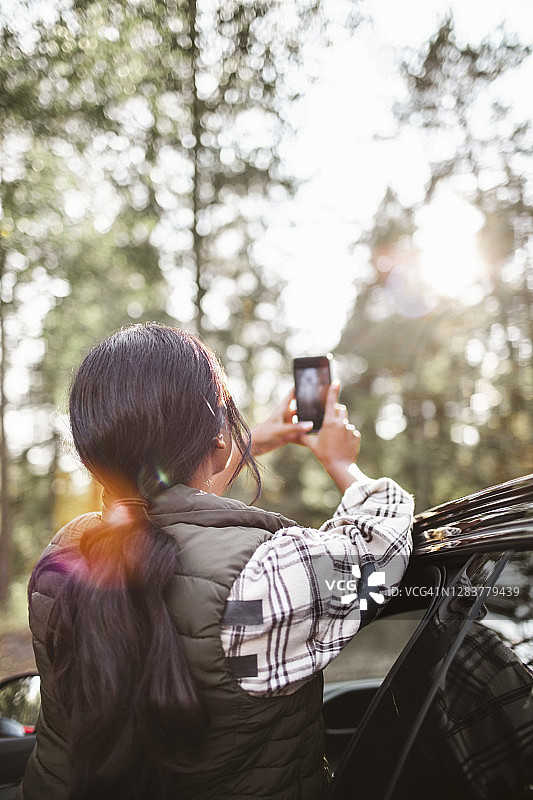度假时女子在车旁用手机拍照的背影图片素材
