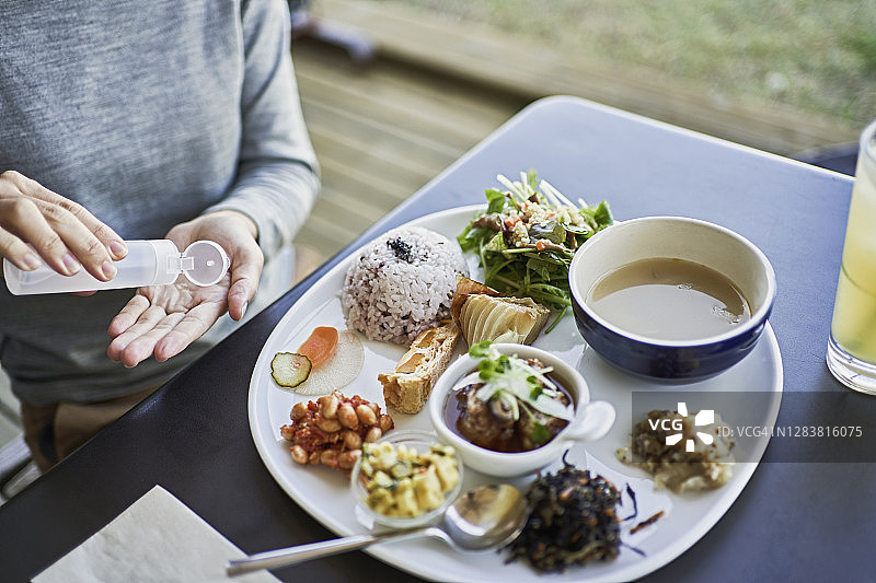 日本女人在纯素咖啡馆用酒精凝胶消毒双手后坐下图片素材