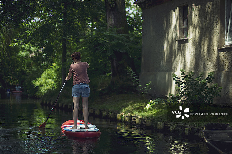 在桨板上漂浮于森林中的年轻女人，德国勃兰登堡州吕贝瑙图片素材