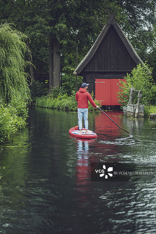 在森林中划桨板的年轻男人，背景是小木屋图片素材