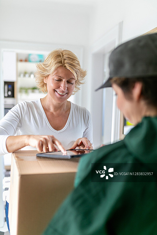 微笑的中年妇女在数字平板电脑上签收快递图片素材