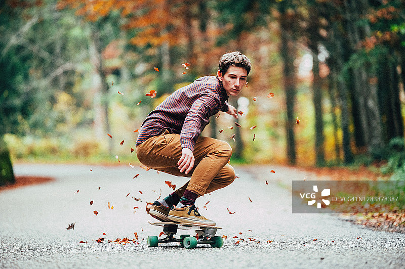 年轻男子踩着滑板穿过马路上的树叶图片素材