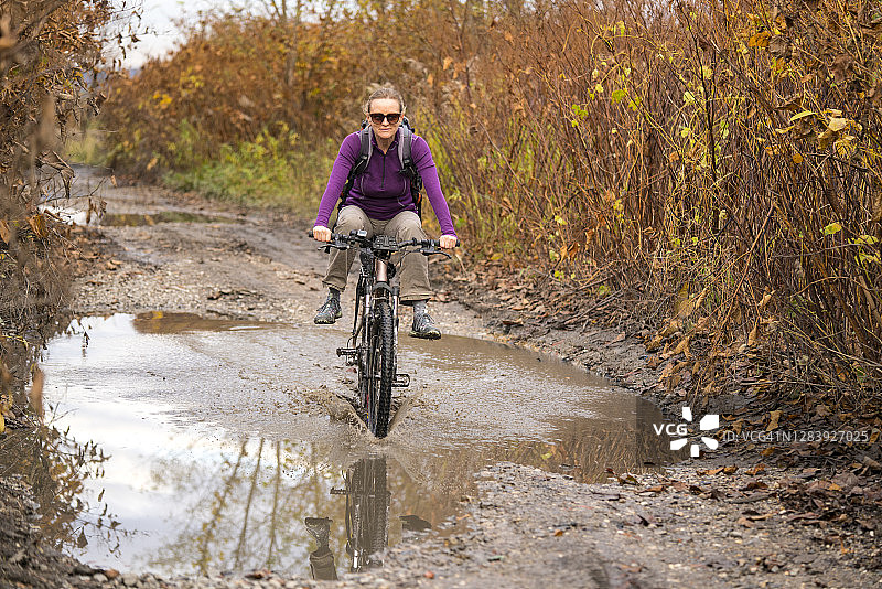 阳光明媚的秋日，中年妇女在泥泞的道路上骑自行车图片素材