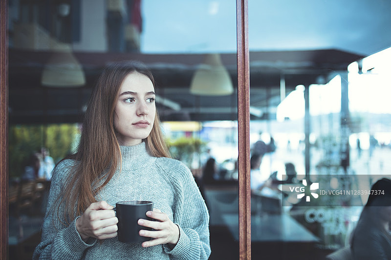 年轻女子手捧咖啡，望向窗外图片素材