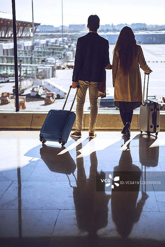 商务情侣在机场候机区拿着行李，望向窗外图片素材