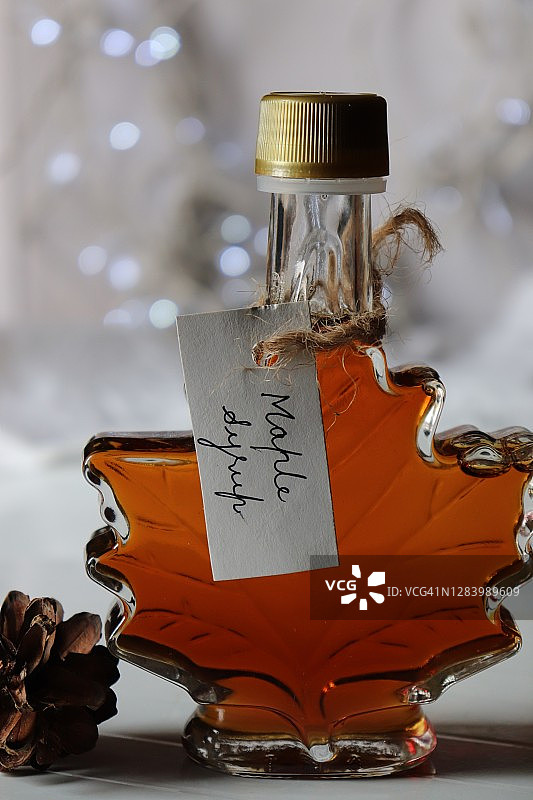 枫叶形瓶装枫糖浆，搭配松果，白色背景和灯光/圣诞节/加拿大图片素材