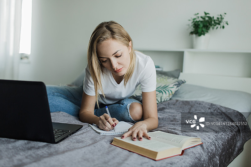 穿着白色T恤和牛仔裤的女学生坐在床上学习写作图片素材