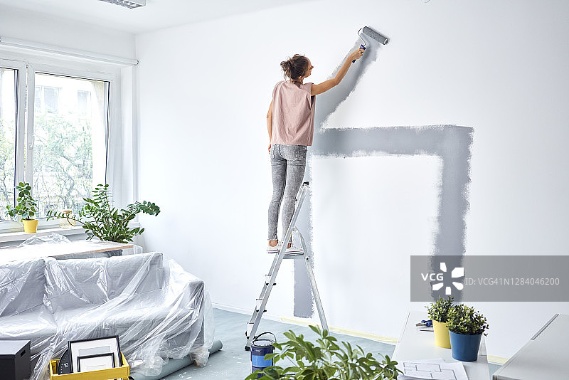 年轻女子站在梯子上用滚筒粉刷墙壁图片素材