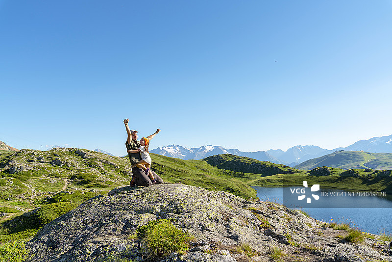 晴朗的一天，父亲单膝跪地，举起双臂与女儿玩耍图片素材