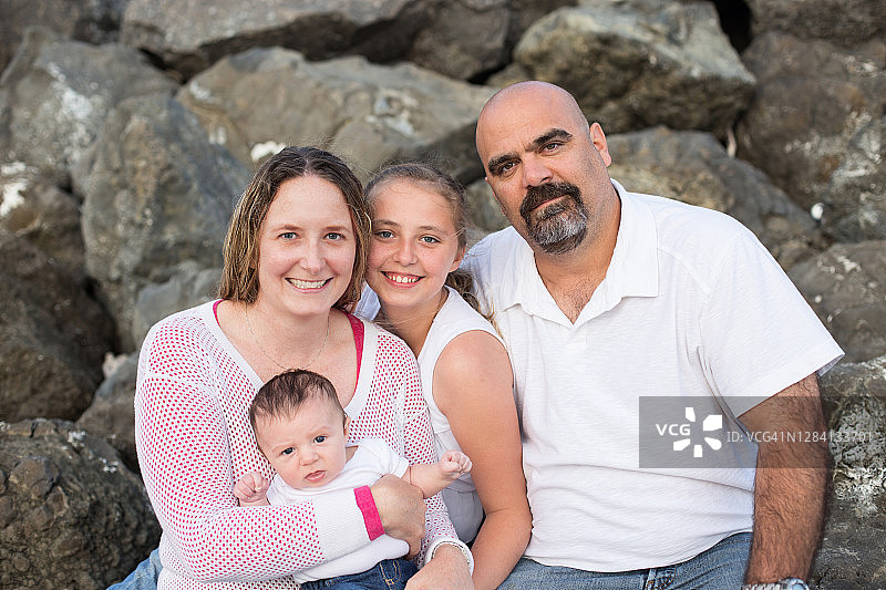 年轻家庭坐在岩石上看着镜头图片素材