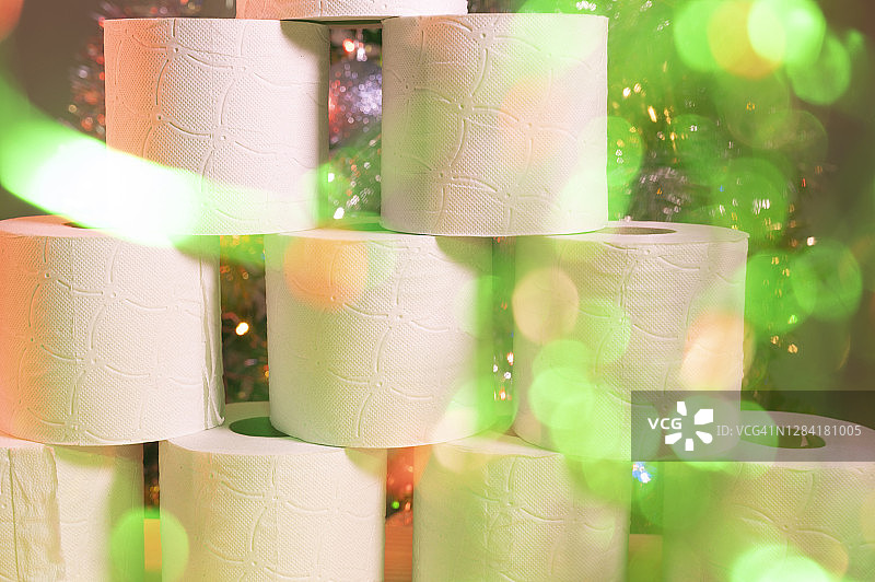 许多卷卫生纸的特写，背景中有一棵装饰着彩色灯光的圣诞树，焦点模糊图片素材