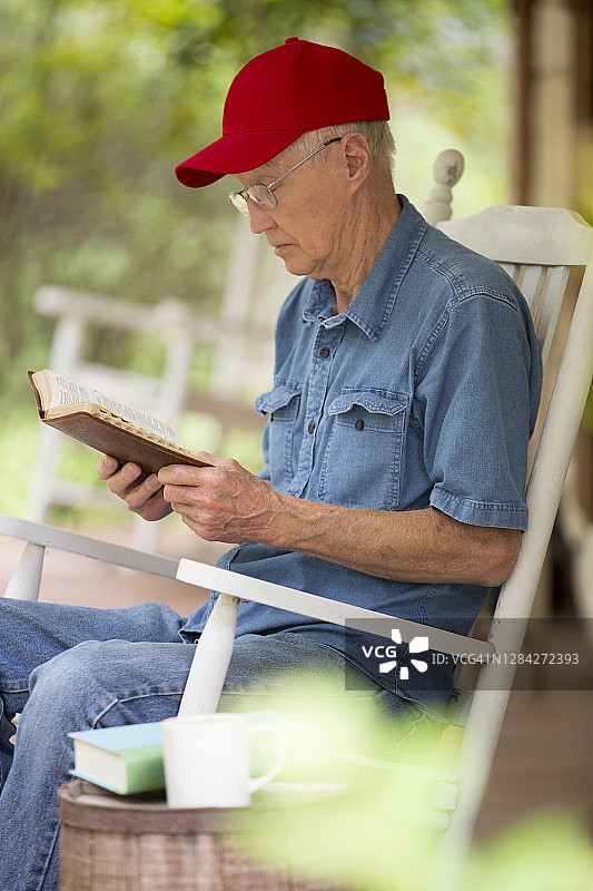 年长的男人坐在门廊的摇椅上读《圣经》图片素材