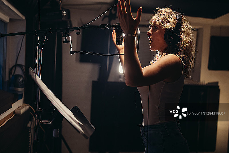 女歌手在录音棚对着麦克风唱歌图片素材