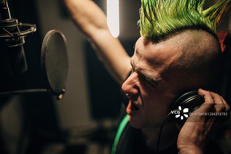 在录音棚里对着麦克风唱歌的朋克男人图片素材